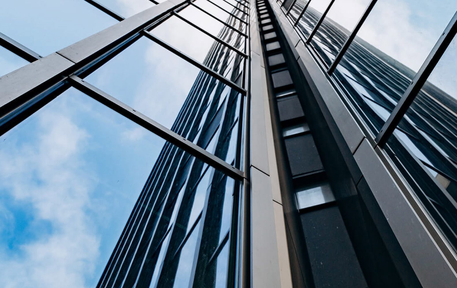 Grattacielo moderno riflette il cielo azzurro, visto dal basso verso l'alto in una prospettiva diagonale.