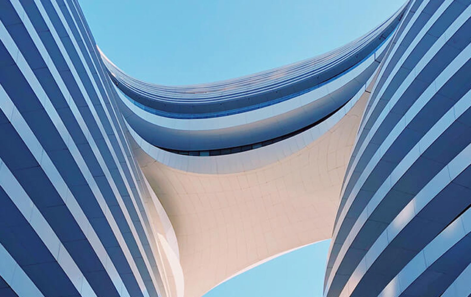 Architettura moderna con curve fluide e linee ondulate sullo sfondo di un cielo blu chiaro.