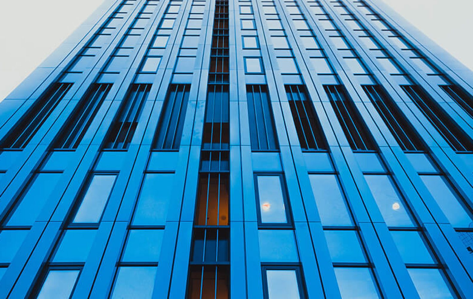 Grattacielo moderno blu, visto dal basso verso l'alto, che si staglia contro il cielo chiaro.