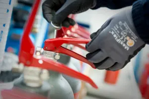 Guanti neri manipolano attrezzature con maniglie rosse in un ambiente industriale dettagliato.