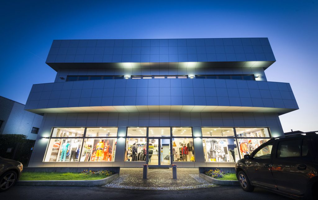 Sede Astra Srl, illuminata di sera, con vetrine che mostrano abbigliamento da lavoro.