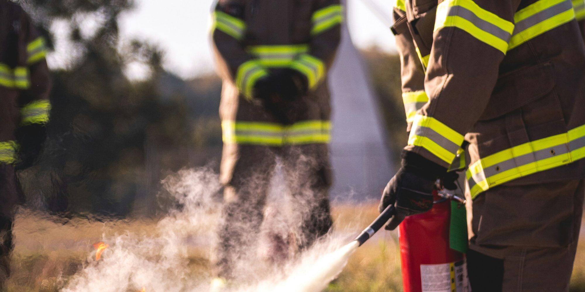 Un pompiere spegne un incendio controllato utilizzando un estintore, mentre colleghi osservano la dimostrazione.
