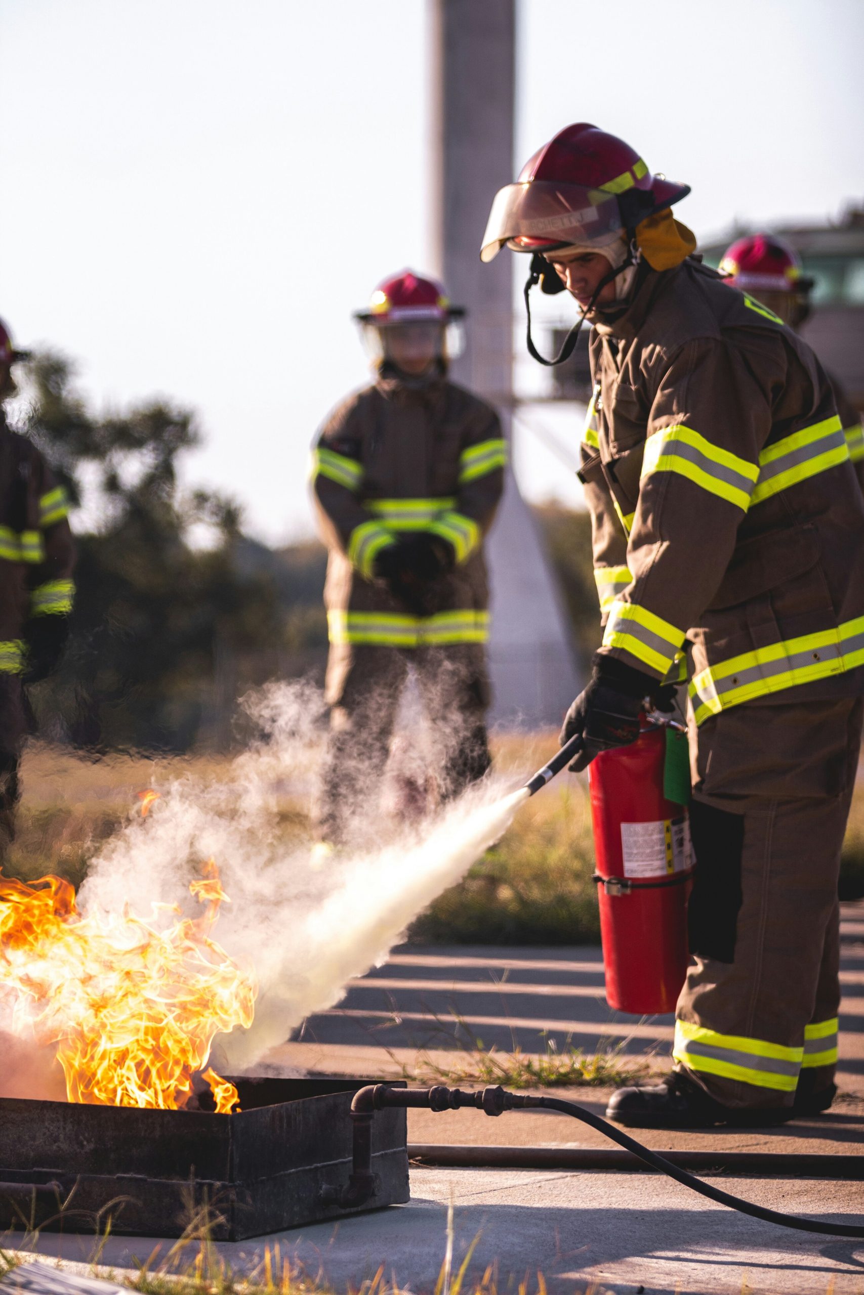 Un pompiere spegne un incendio controllato utilizzando un estintore, mentre colleghi osservano la dimostrazione.
